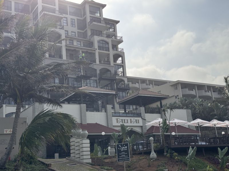 Exterior view of the Bali Hai apartment complex featuring multi-level balconies, tiled roofing, and an integrated restaurant area at the base.
