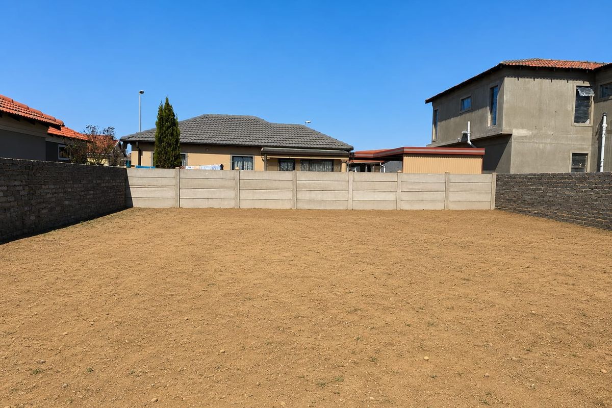 A level, vacant residential plot enclosed by precast concrete and brick boundary walls, situated in a developed suburban neighborhood.