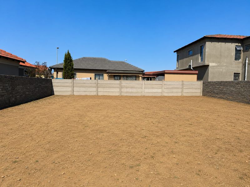 A level, vacant residential plot enclosed by precast concrete and brick boundary walls, situated in a developed suburban neighborhood.