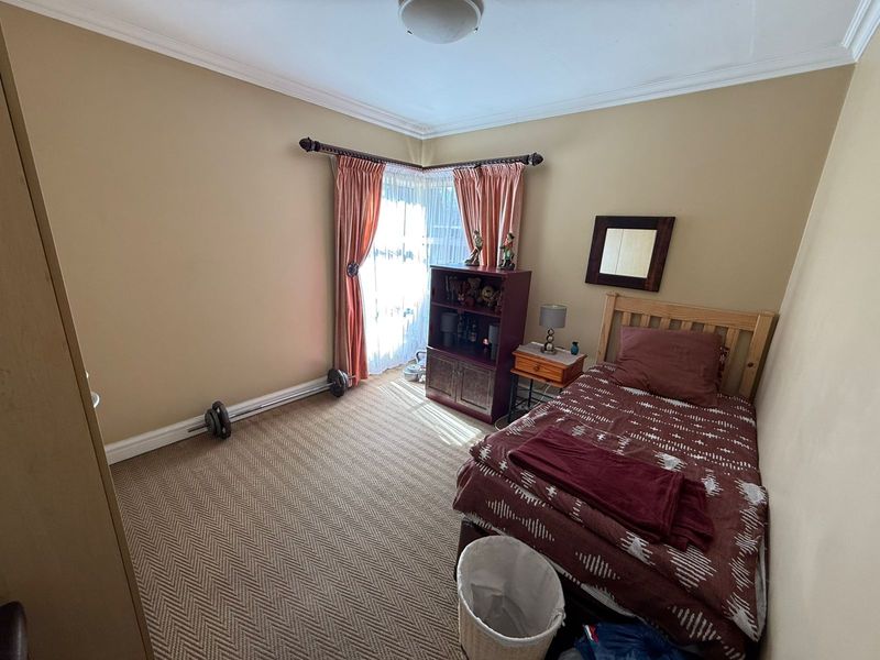 A functional bedroom featuring neutral wall tones, carpeted flooring, and decorative cornice detailing, providing a comfortable and well-proportioned living space.