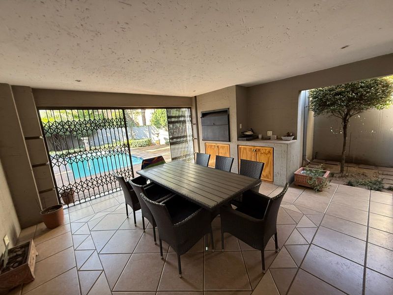 Covered patio area featuring a built-in braai, tiled flooring, and direct access to the pool area through security gates.