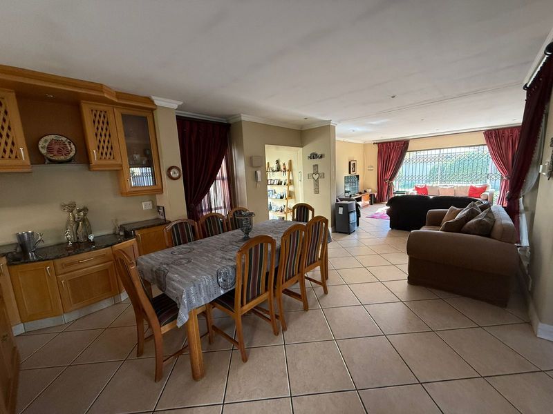 Spacious open-plan living and dining area featuring tiled flooring, built-in cabinetry with granite countertops, and large windows with security bars.
