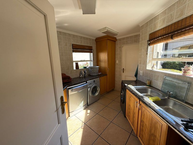 Functional laundry room featuring built-in wooden cabinetry, granite countertops, tiled splashbacks, and integrated plumbing for appliances.