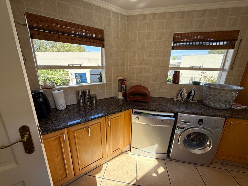 A functional laundry area featuring granite countertops, wooden cabinetry, tiled splashbacks, and dedicated space for a dishwasher and washing machine.