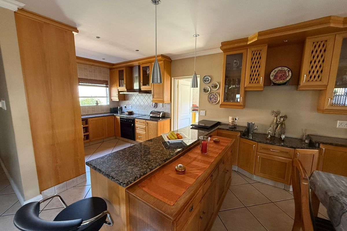 A spacious kitchen featuring wooden cabinetry, granite countertops, a central island, and tiled flooring, offering a functional layout with ample storage space.