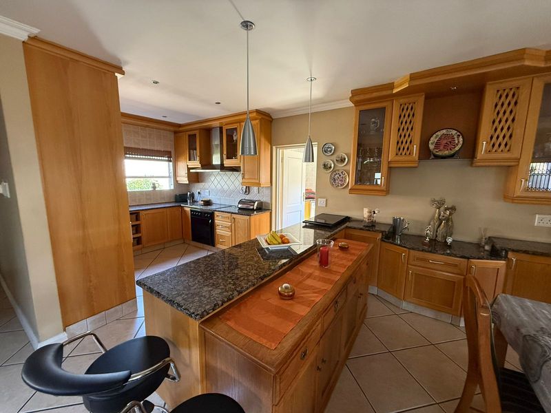A spacious kitchen featuring wooden cabinetry, granite countertops, a central island, and tiled flooring, offering a functional layout with ample storage space.