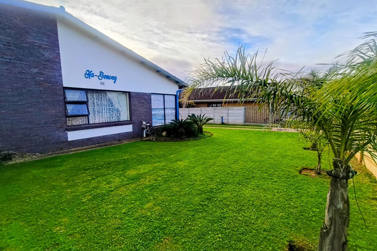 A well-maintained rear garden featuring a spacious lawn, brick exterior wall, and secure precast concrete boundary fencing.