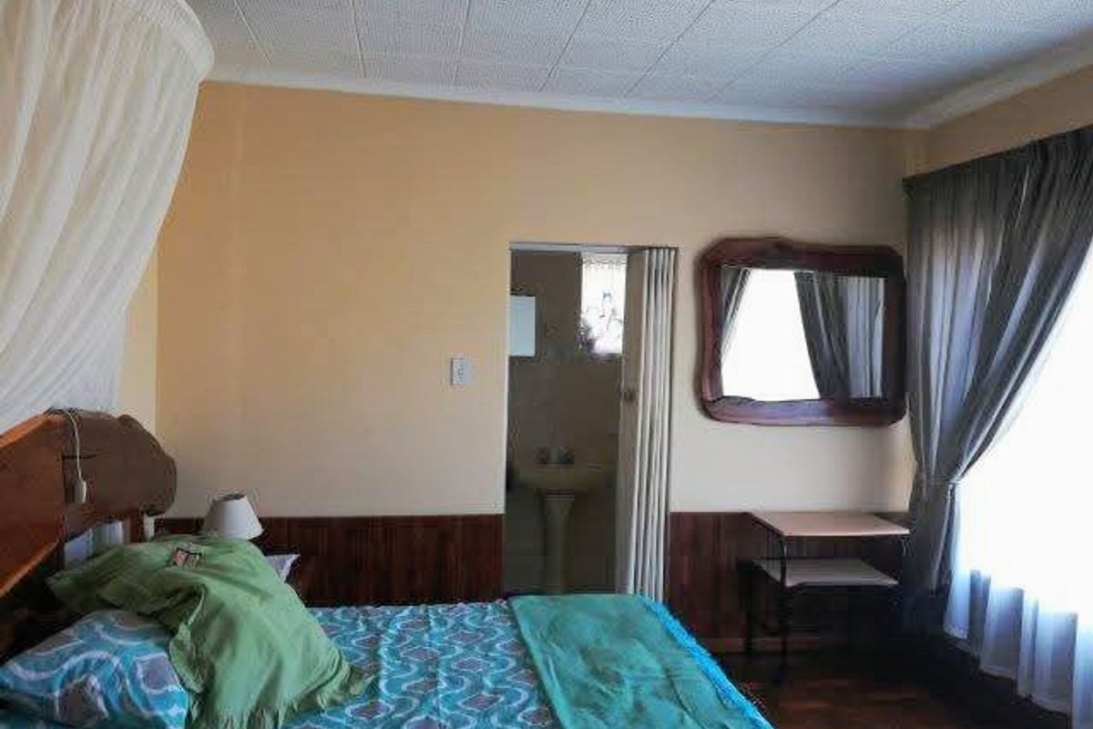 Bedroom featuring parquet flooring, wood wall paneling, and an en-suite bathroom with a folding door entry.