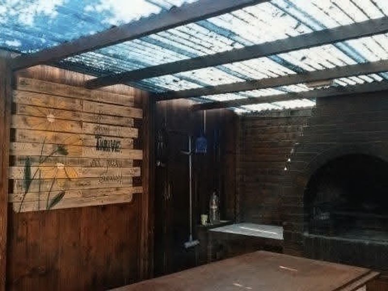 Covered outdoor patio area featuring a built-in brick fireplace and timber wall cladding, providing a rustic space for outdoor entertaining.