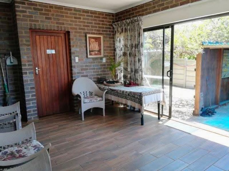 A covered patio area featuring exposed brick walls, wood-look tiled flooring, and large sliding glass doors providing direct access to the outdoor pool area.