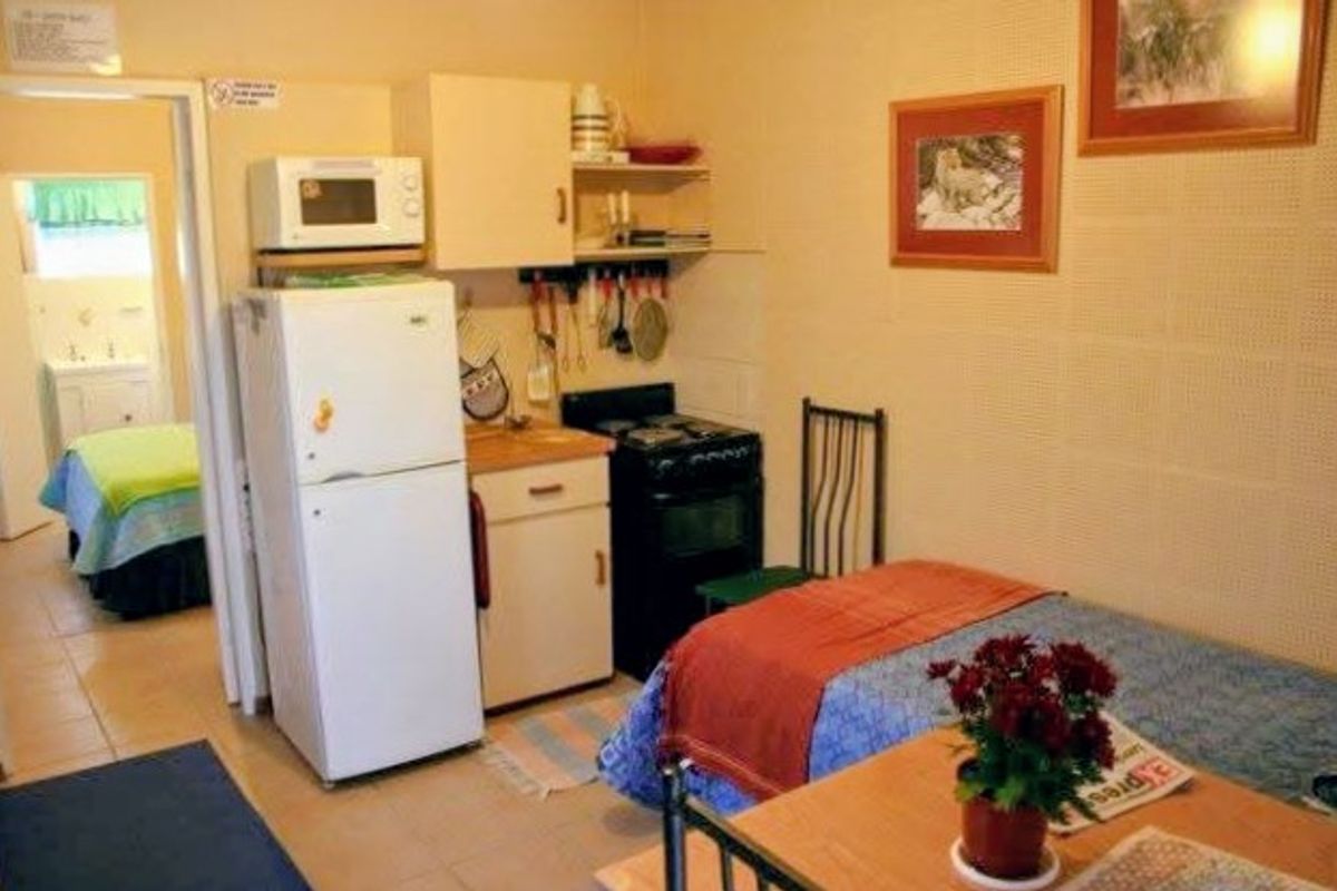 A compact kitchenette area featuring basic cabinetry, a freestanding stove, and a microwave, with direct access to an adjacent bedroom.