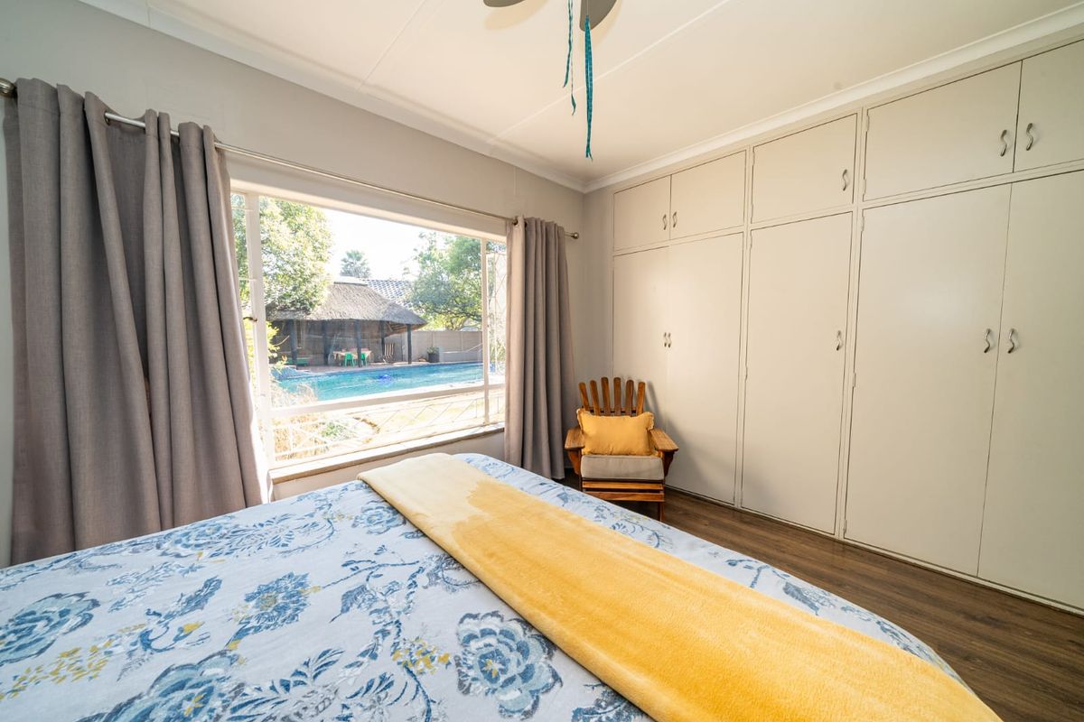 A well-lit bedroom featuring extensive built-in cupboards, laminate flooring, a ceiling fan, and a large window overlooking the pool area.
