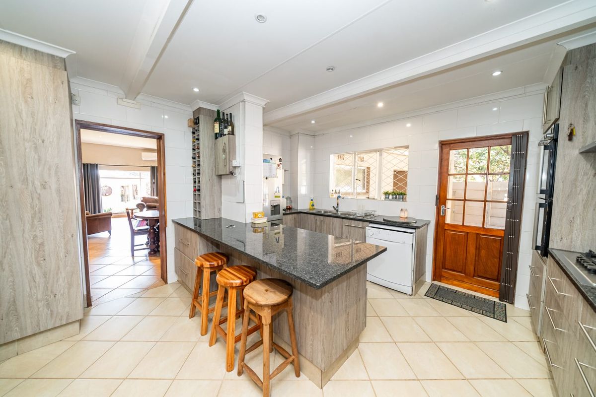 Modern kitchen featuring granite countertops, ample built-in cabinetry, a breakfast bar, and integrated appliances, with direct access to the living area.