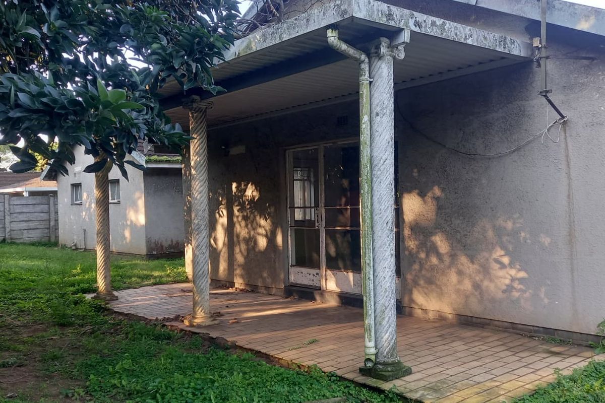 Rear exterior view of the house featuring a covered patio with decorative columns, tiled flooring, and a sliding glass door entrance.