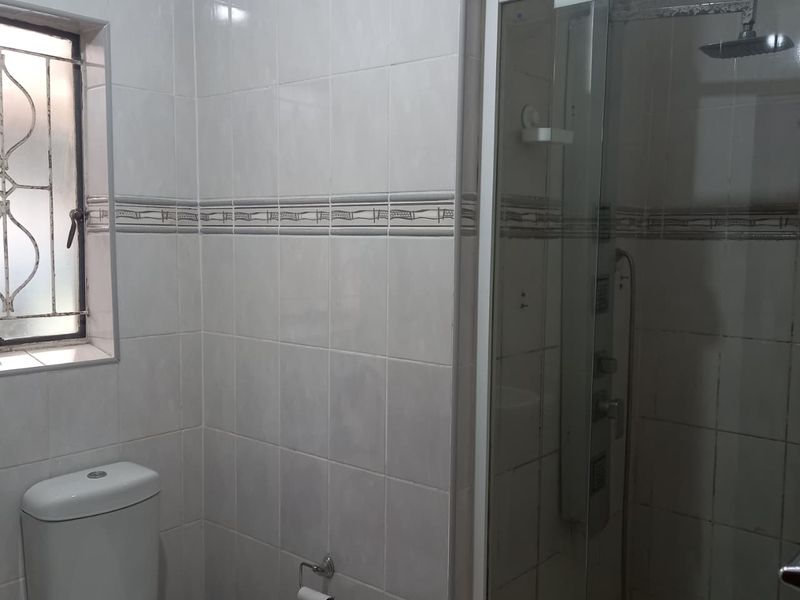 A functional bathroom featuring a glass-enclosed shower, white ceramic toilet, and neutral wall tiling with decorative border accents.