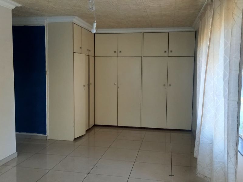 A vacant bedroom featuring extensive built-in cupboard storage, tiled flooring, and a textured ceiling finish.