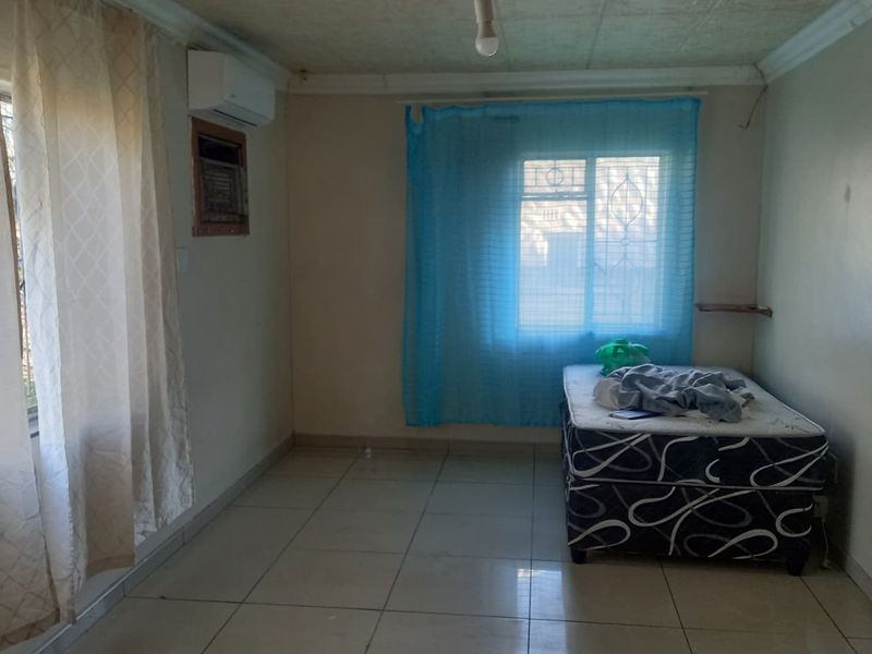 A bedroom featuring tiled flooring, an air conditioning unit, and security bars on the window, with a textured ceiling and basic lighting.