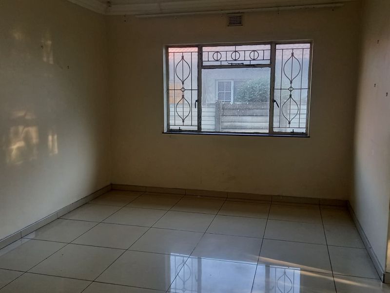 An empty bedroom featuring tiled flooring, a ceiling light fixture, and a window fitted with security bars.