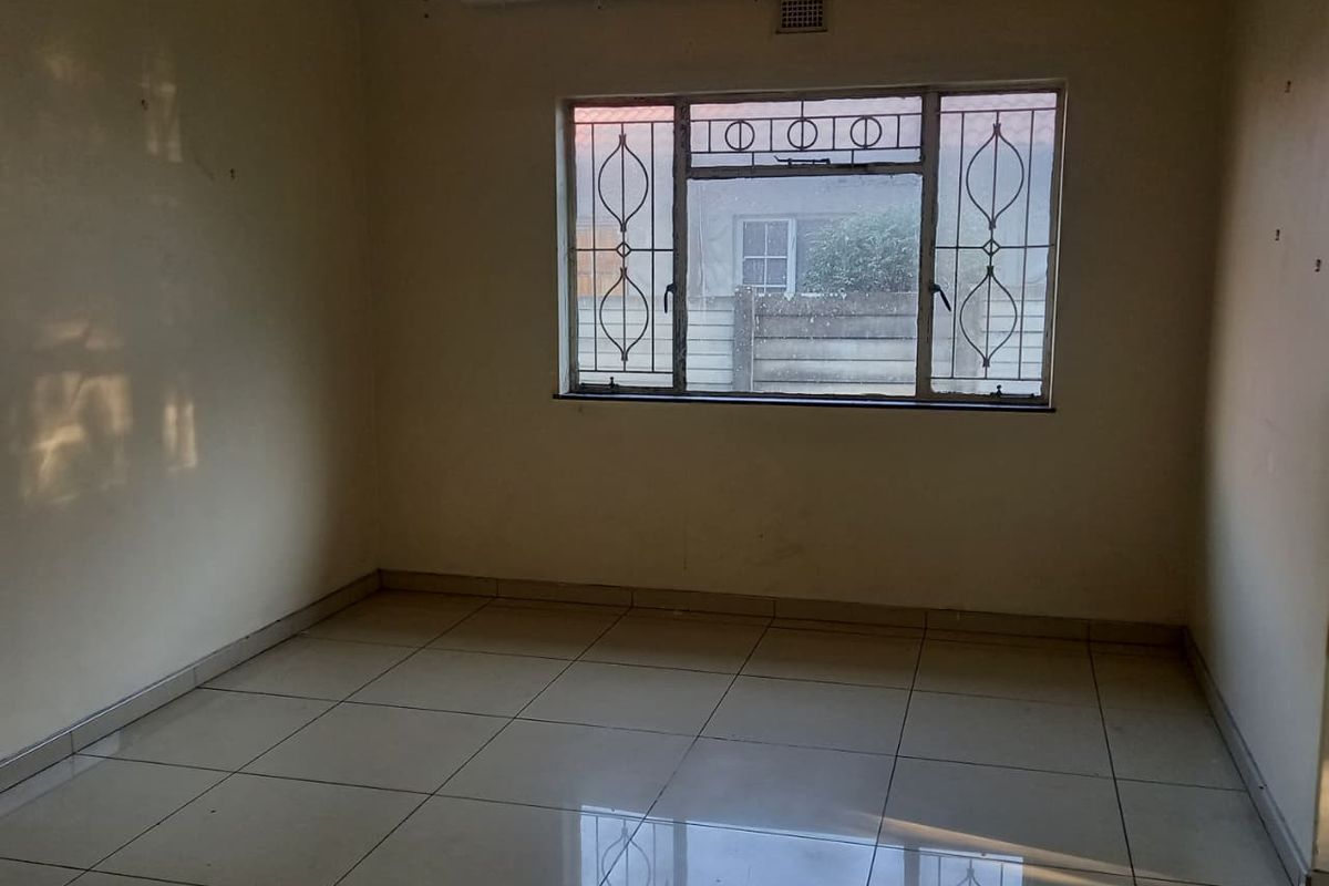 An empty bedroom featuring tiled flooring, a ceiling light fixture, and a window fitted with security bars.
