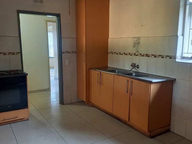 A functional kitchen featuring built-in cabinetry, a stainless steel double sink, tiled splashbacks, and ceramic floor tiles, ready for modernization.
