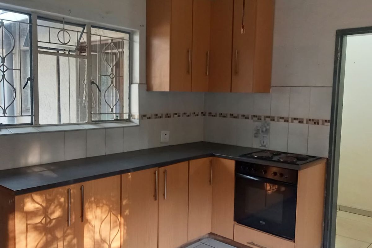 A functional kitchen featuring laminate cabinetry, built-in oven, electric hob, and tiled splashback, offering a practical layout ready for modernization.