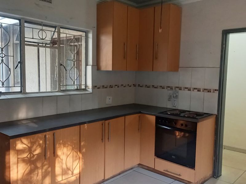 A functional kitchen featuring laminate cabinetry, built-in oven, electric hob, and tiled splashback, offering a practical layout ready for modernization.