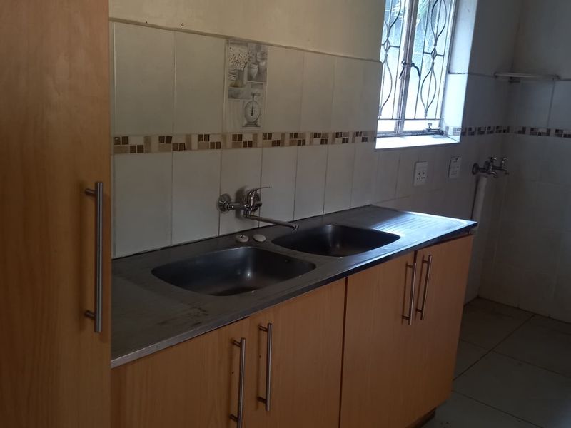 A functional kitchen area featuring a double stainless steel sink, tiled backsplash, and laminate cabinetry, offering a blank canvas for potential renovation.