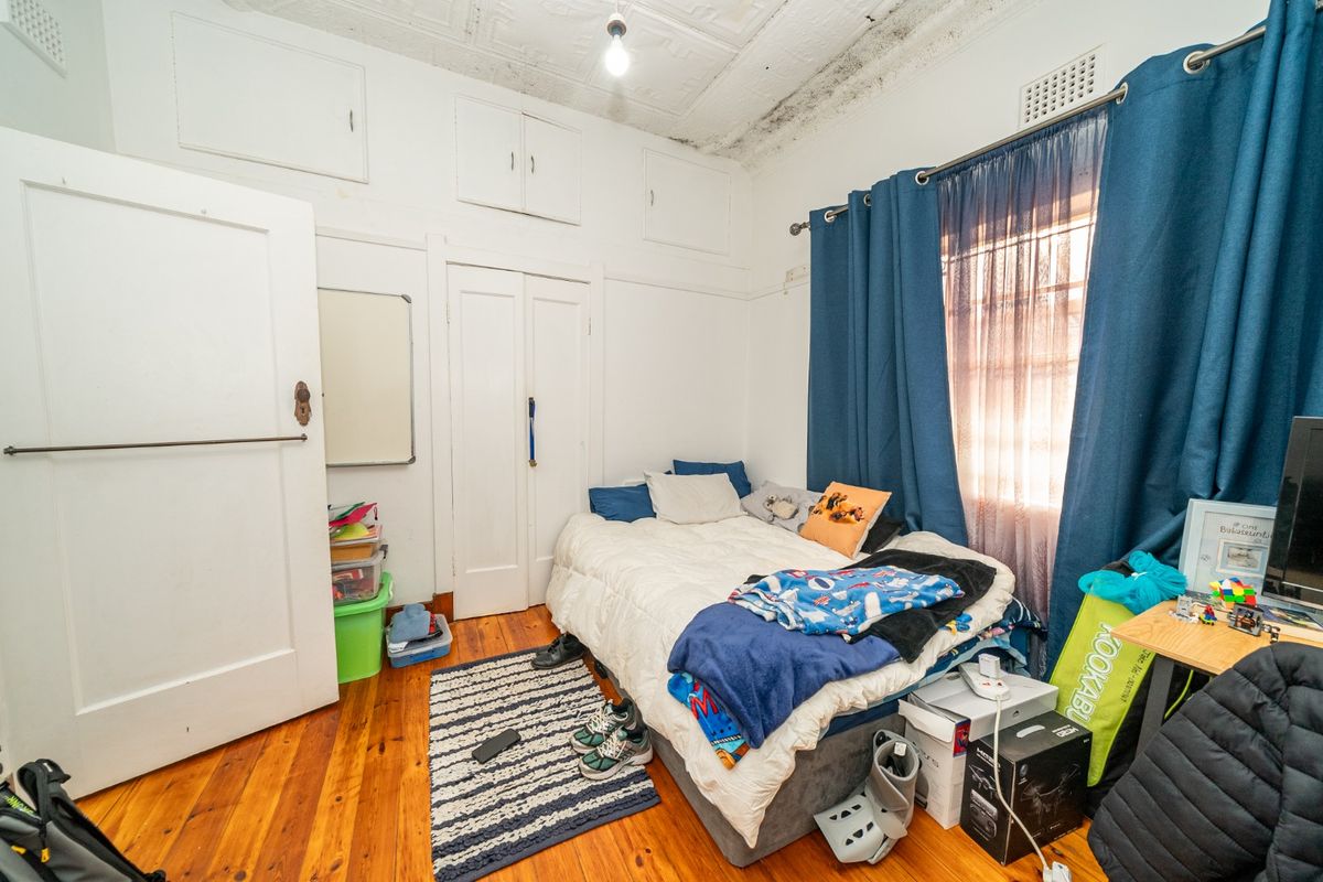 A bedroom featuring original timber flooring and a pressed metal ceiling, currently showing signs of significant moisture damage and mold on the upper walls.
