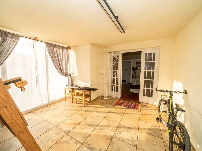 A covered patio area featuring tiled flooring, a security gate, and access to the interior through glass panel doors.