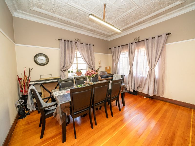 A well-maintained dining room featuring original hardwood flooring, classic picture rails, and an ornate pressed metal ceiling, offering a charming period aesthetic.