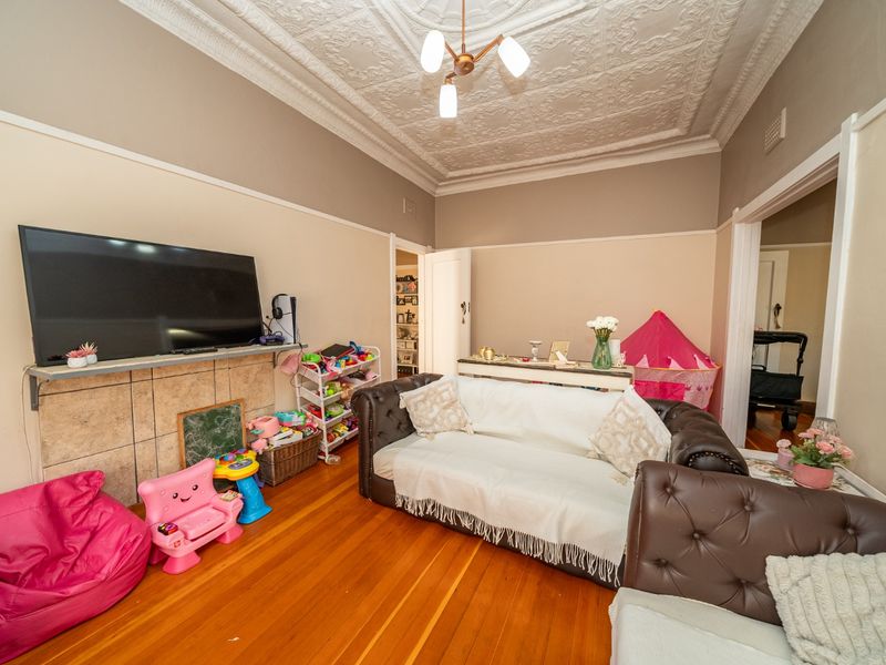 A living room featuring original ornate pressed metal ceilings, polished timber flooring, and a tiled fireplace surround, offering classic character and charm.