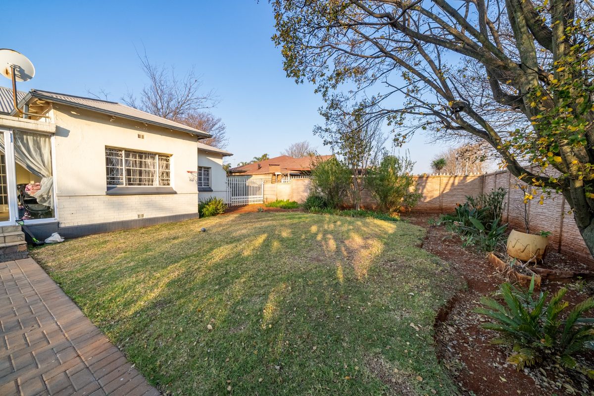 A rear garden view featuring a lawn area, paved walkway, and perimeter boundary wall, with a side view of the house exterior.
