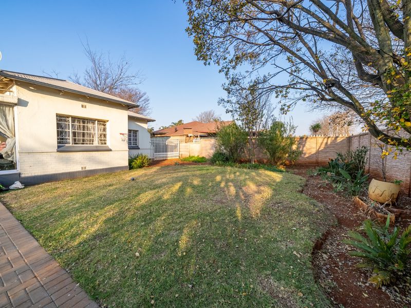 A rear garden view featuring a lawn area, paved walkway, and perimeter boundary wall, with a side view of the house exterior.