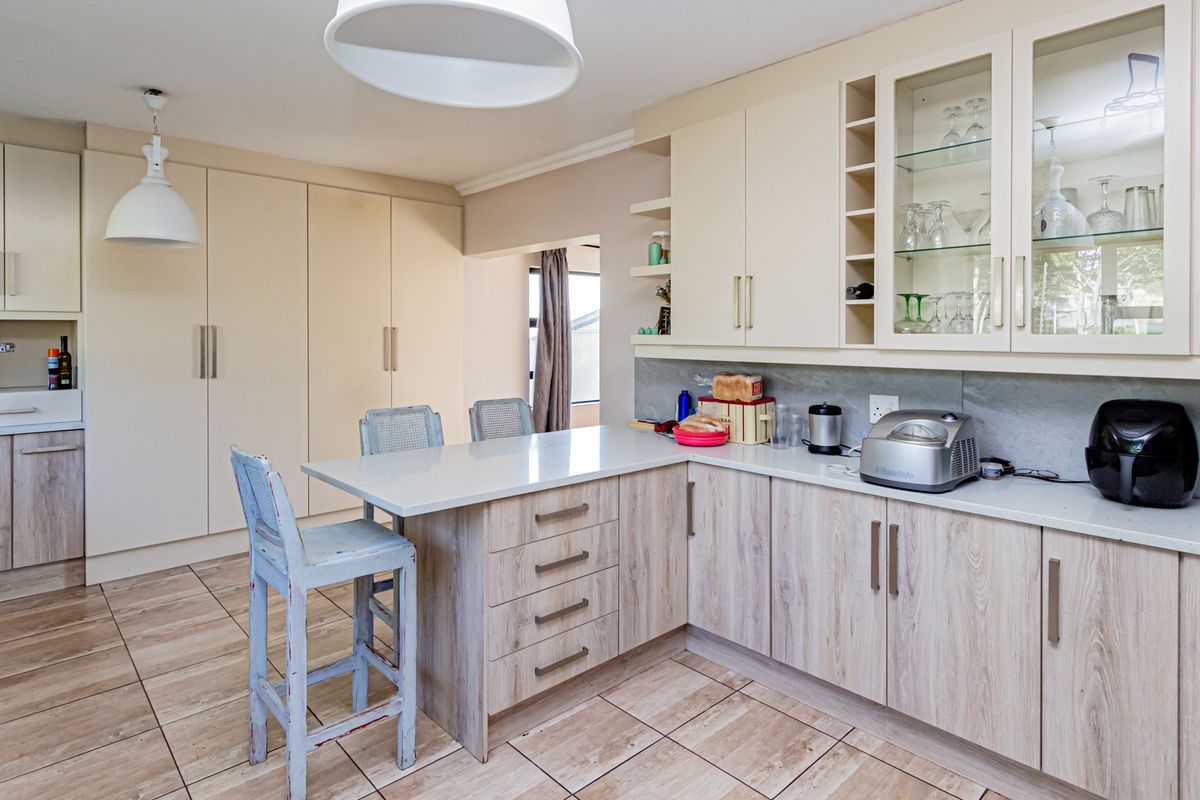 A well-maintained kitchen featuring light wood-grain cabinetry, stone countertops, integrated storage, and tiled flooring with a functional breakfast nook area.