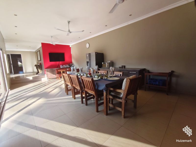 Spacious dining area featuring tiled flooring, ceiling fans, and a distinct red accent wall, providing an open and functional space for family meals.