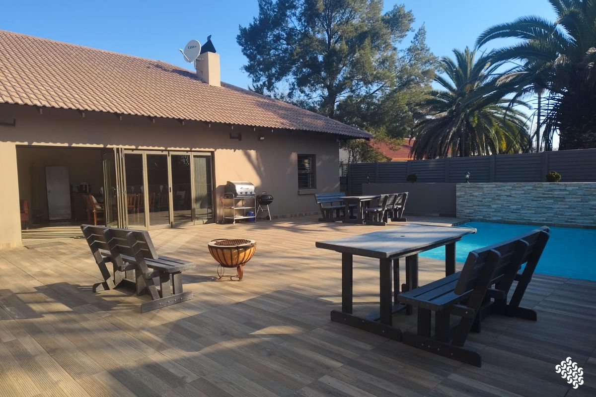 Spacious rear patio featuring wood-look tiling, a swimming pool with a stone feature wall, and large stacking doors leading into the home.
