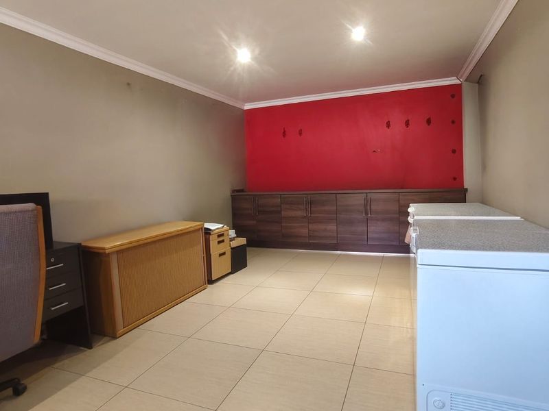 A functional scullery or utility area featuring tiled flooring, built-in dark wood cabinetry, and recessed lighting, currently used for storage.