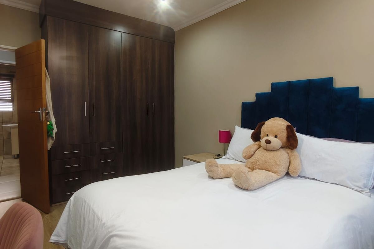 A well-maintained bedroom featuring dark wood built-in wardrobes, a modern ceiling fan, and laminate flooring, with an adjoining view into the bathroom.