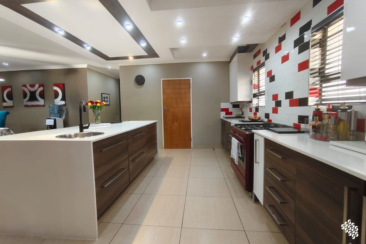 Modern kitchen featuring a large central island, dark wood cabinetry, stone countertops, and a striking red and black tiled backsplash.