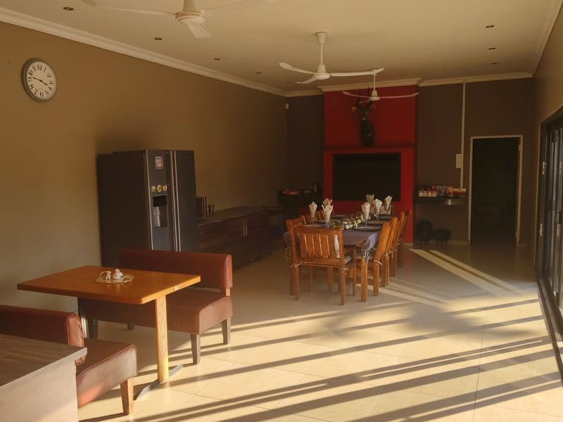 Spacious open-plan living and dining area featuring tiled floors, ceiling fans, and a prominent fireplace, illuminated by natural light from large sliding doors.