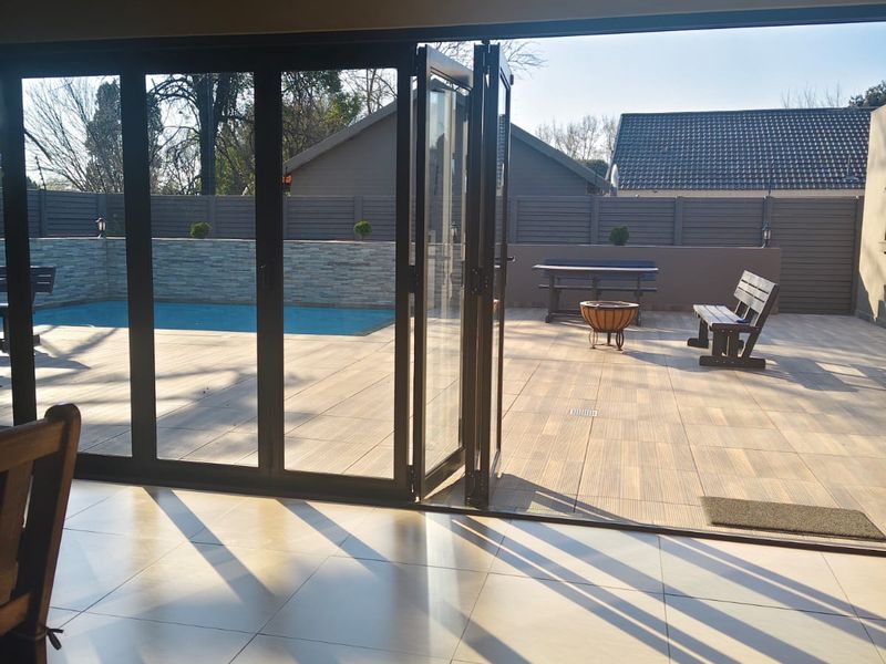 Open plan living area featuring large bi-fold doors opening onto a spacious outdoor deck with a swimming pool and stone-clad feature wall.