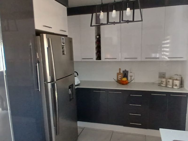 Modern kitchen featuring high-gloss cabinetry, stone countertops, and contemporary pendant lighting, offering a clean and functional workspace.
