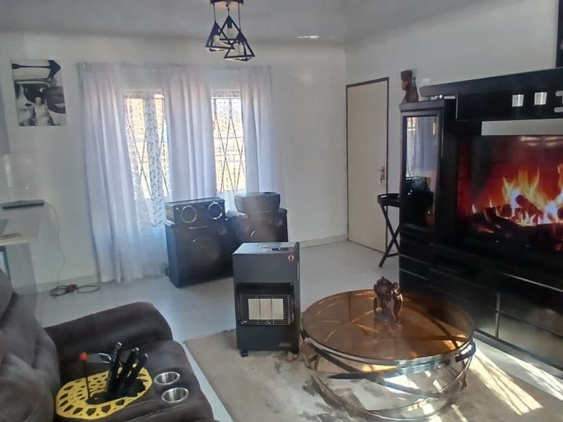 Open plan living area featuring tiled flooring, modern pendant lighting, and security bars on windows, creating a functional and connected living space.