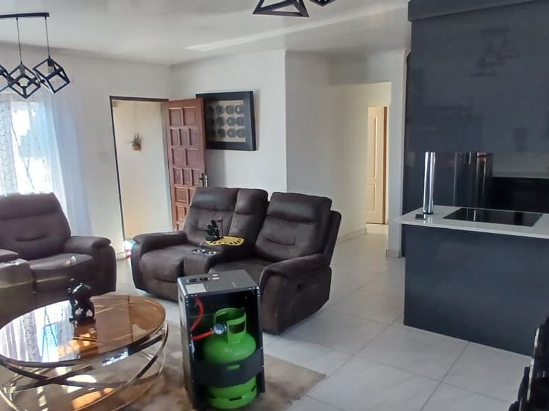 An open-plan living and kitchen area featuring modern dark cabinetry, a kitchen island with a hob, and neutral tiled flooring throughout.