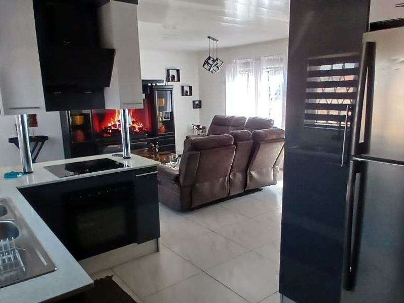 Modern open-plan kitchen and living area featuring sleek cabinetry, integrated appliances, tiled flooring, and a cozy fireplace in the lounge section.