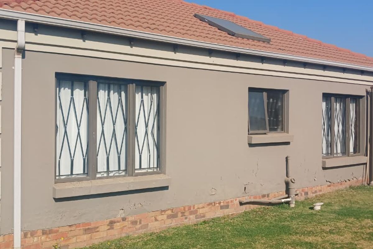 Rear elevation of a single-story house featuring a tiled roof with solar water heater, security bars on windows, and visible exterior wall maintenance requirements.