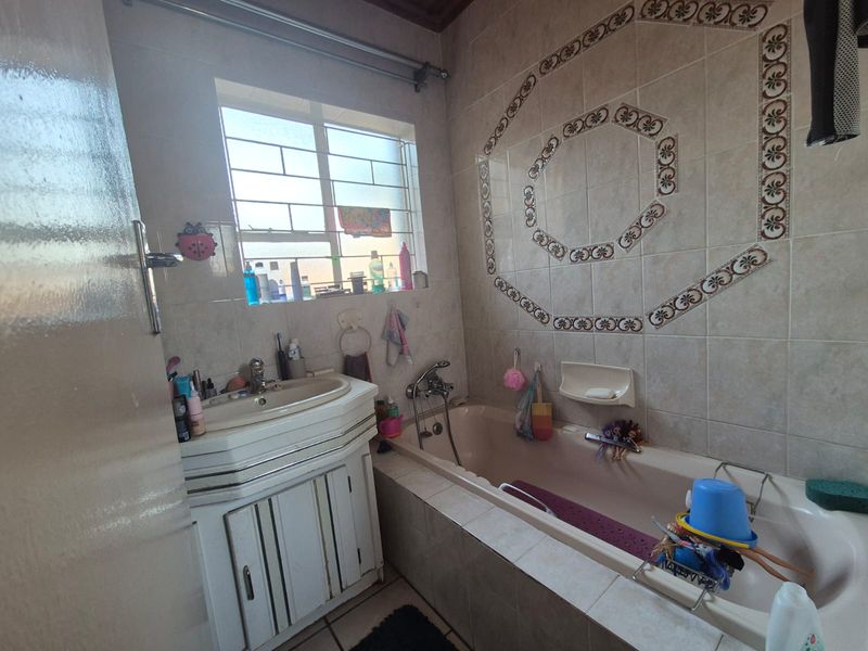 A functional bathroom featuring a built-in vanity with basin, a tiled bathtub surround, and decorative wall tiling.