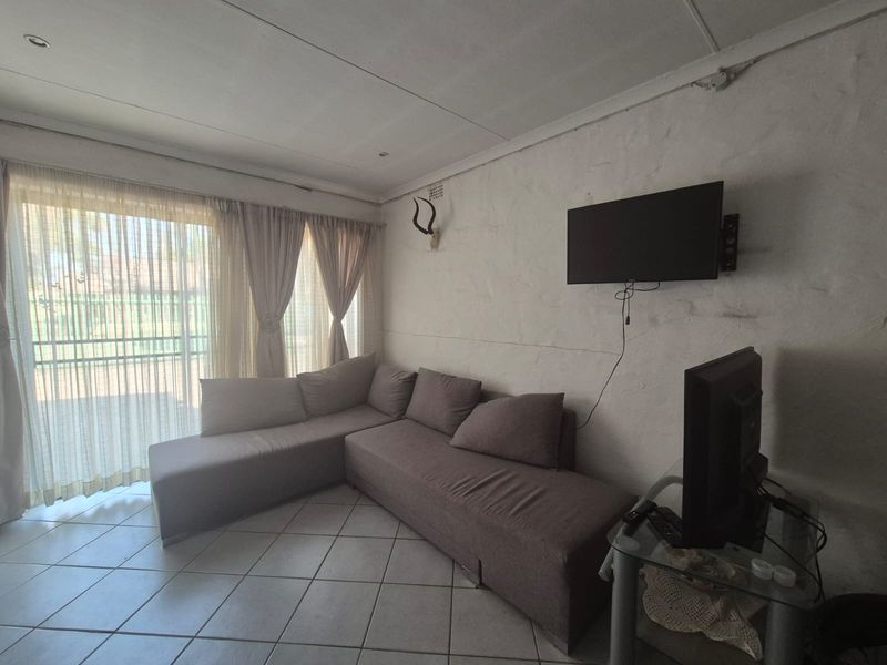 A living room featuring tiled flooring and a sliding glass door leading to an outdoor area, with wall-mounted television infrastructure.