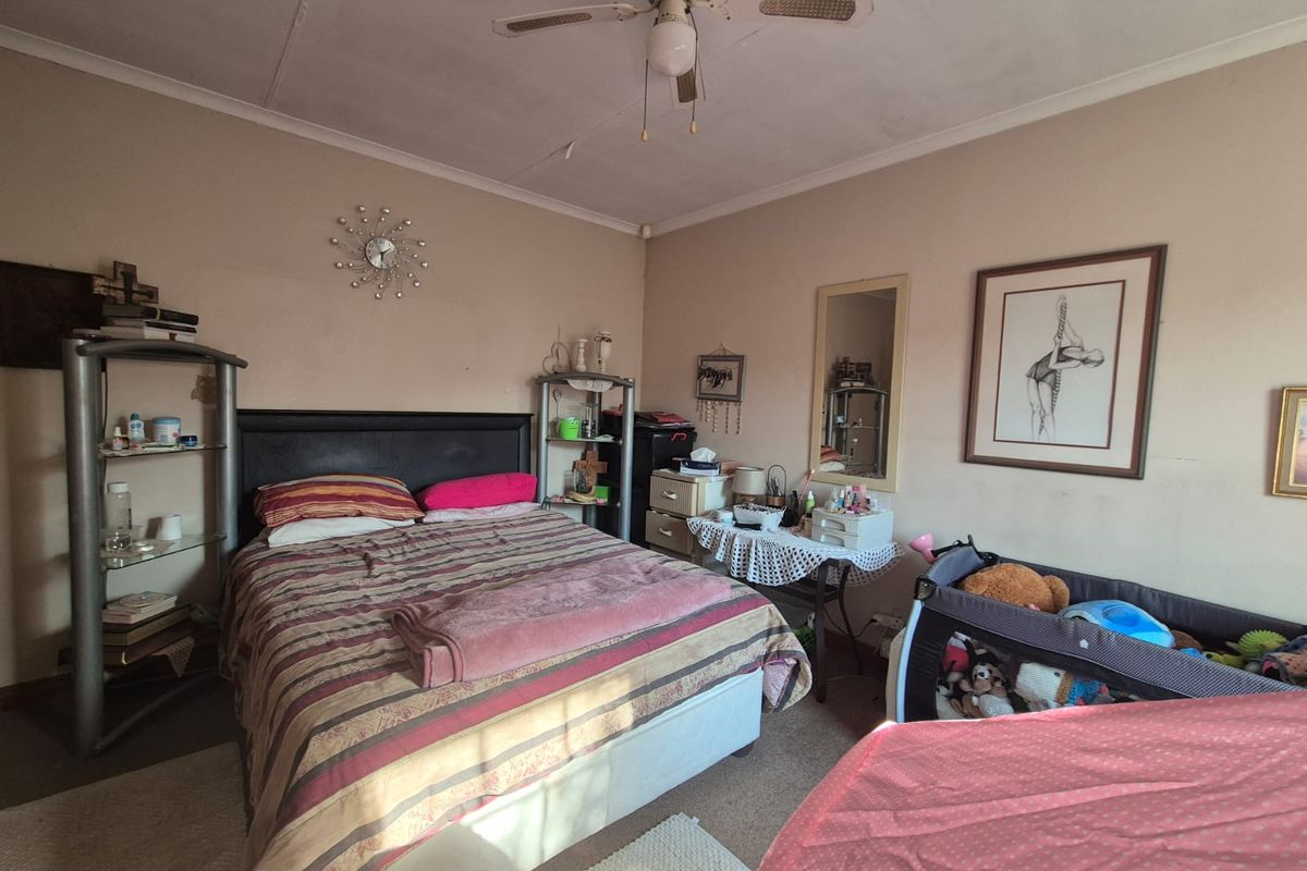 A bedroom featuring a ceiling fan, with visible wear on the walls and ceiling requiring maintenance.
