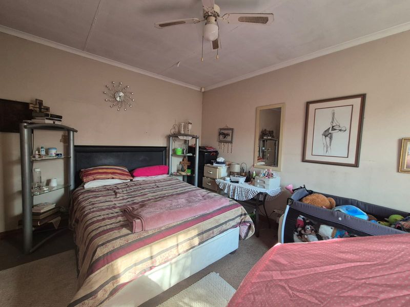 A bedroom featuring a ceiling fan, with visible wear on the walls and ceiling requiring maintenance.